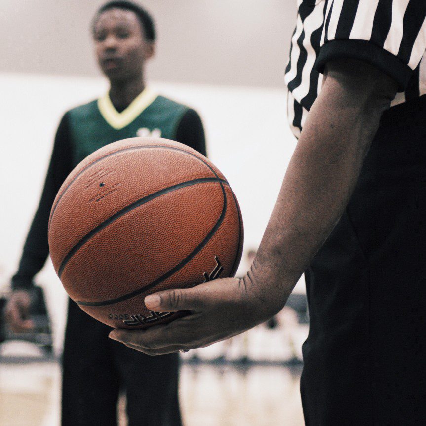 A referee holding a basketball in front of another player.