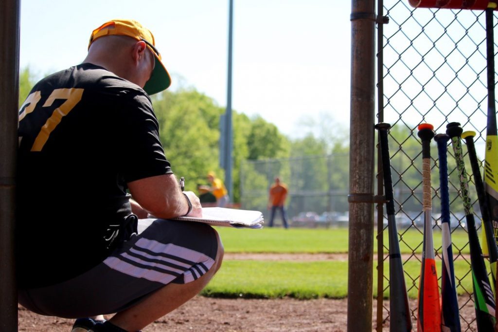 A man in black shirt holding baseball bat near fence.