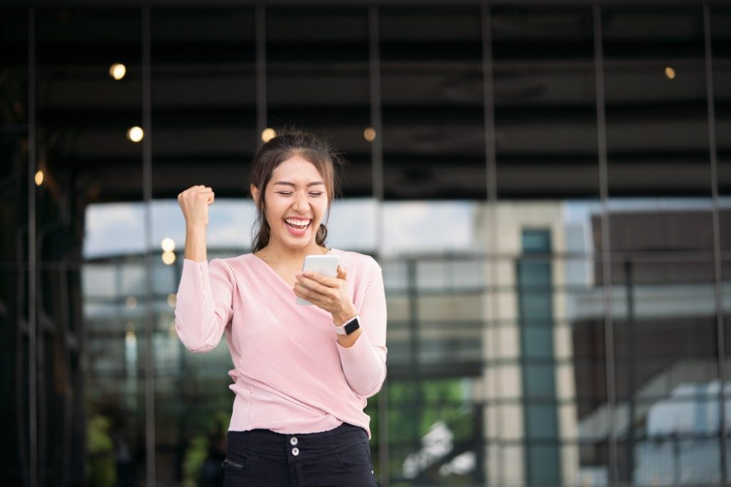 A woman is holding her arms up and looking at the phone.