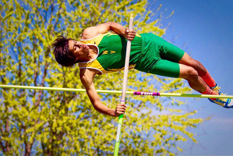 A man in green and yellow jumping over a pole.