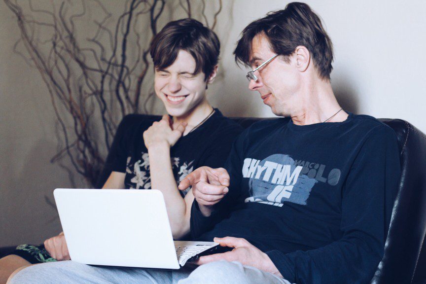 Two people sitting on a couch looking at a laptop.