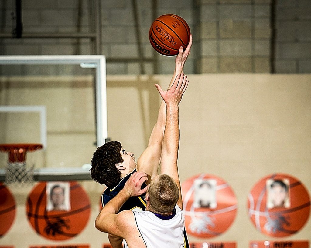 Two men playing basketball on a court with orange walls.